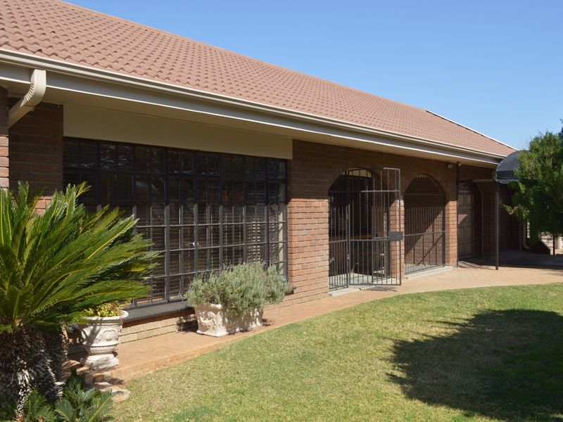 Rear view of a brick house featuring a tiled roof, steel-framed windows with security bars, and a paved walkway leading along the garden.