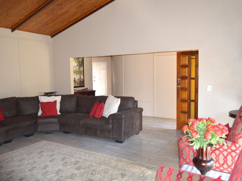 Spacious living room featuring a vaulted timber ceiling, neutral wall finishes, and tiled flooring, with a solid timber door leading to an adjacent area.