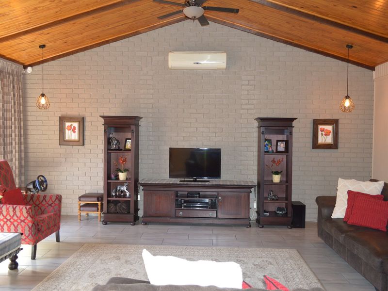 Spacious living room featuring a high raked timber ceiling, exposed brick feature wall, tiled flooring, and integrated split system air conditioning.