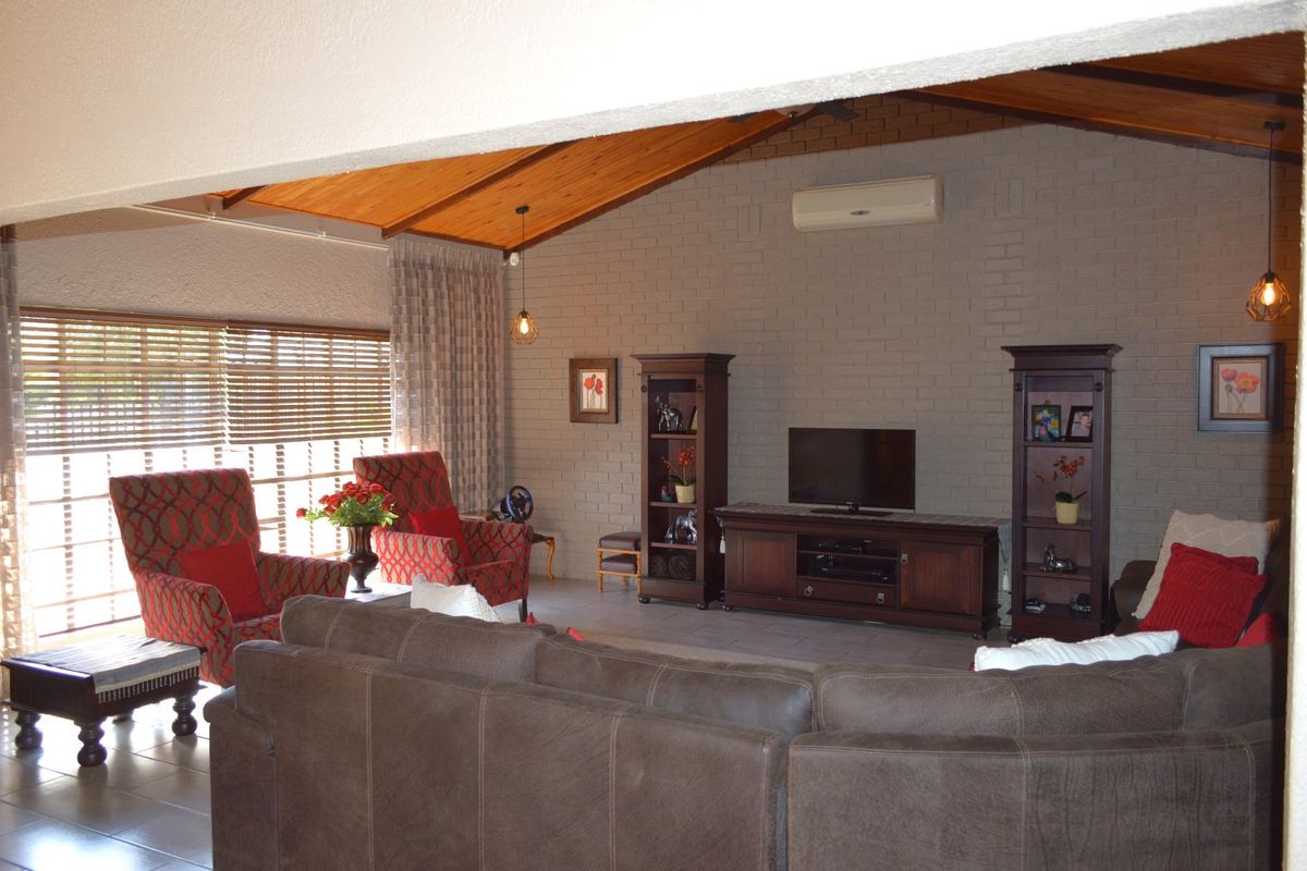 Spacious living room featuring a high exposed timber ceiling, brick feature wall, tiled flooring, and a wall-mounted air conditioning unit.