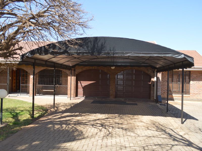Front exterior view featuring a double garage with a large arched carport, brick paved driveway, and secure gated entrance.