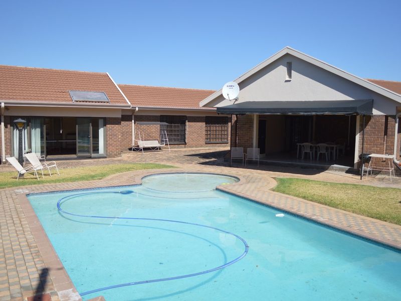 Spacious rear garden featuring a swimming pool, paved patio area, and a covered outdoor entertainment space with a retractable awning.