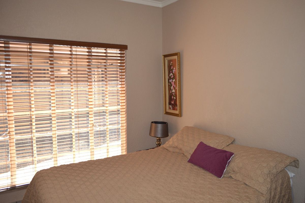 A bedroom featuring neutral wall tones and fitted wooden venetian blinds, providing a simple and functional living space.