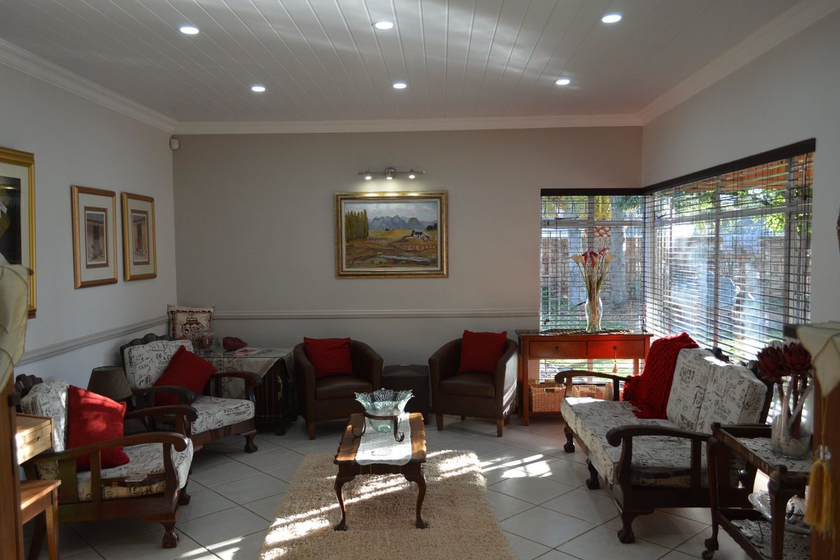A well-lit living room featuring ceramic floor tiles, a tongue and groove ceiling with recessed lighting, and a corner window with venetian blinds.