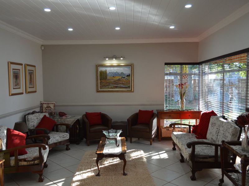 A well-lit living room featuring ceramic floor tiles, a tongue and groove ceiling with recessed lighting, and a corner window with venetian blinds.