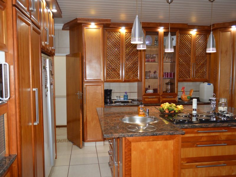 A traditional kitchen featuring extensive wooden cabinetry, granite countertops, a central island with a built-in hob, and tiled flooring.