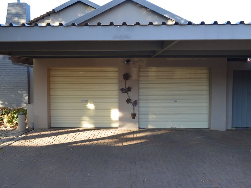 A double garage with roller doors, featuring a paved driveway and a covered carport structure, providing secure off-street parking.