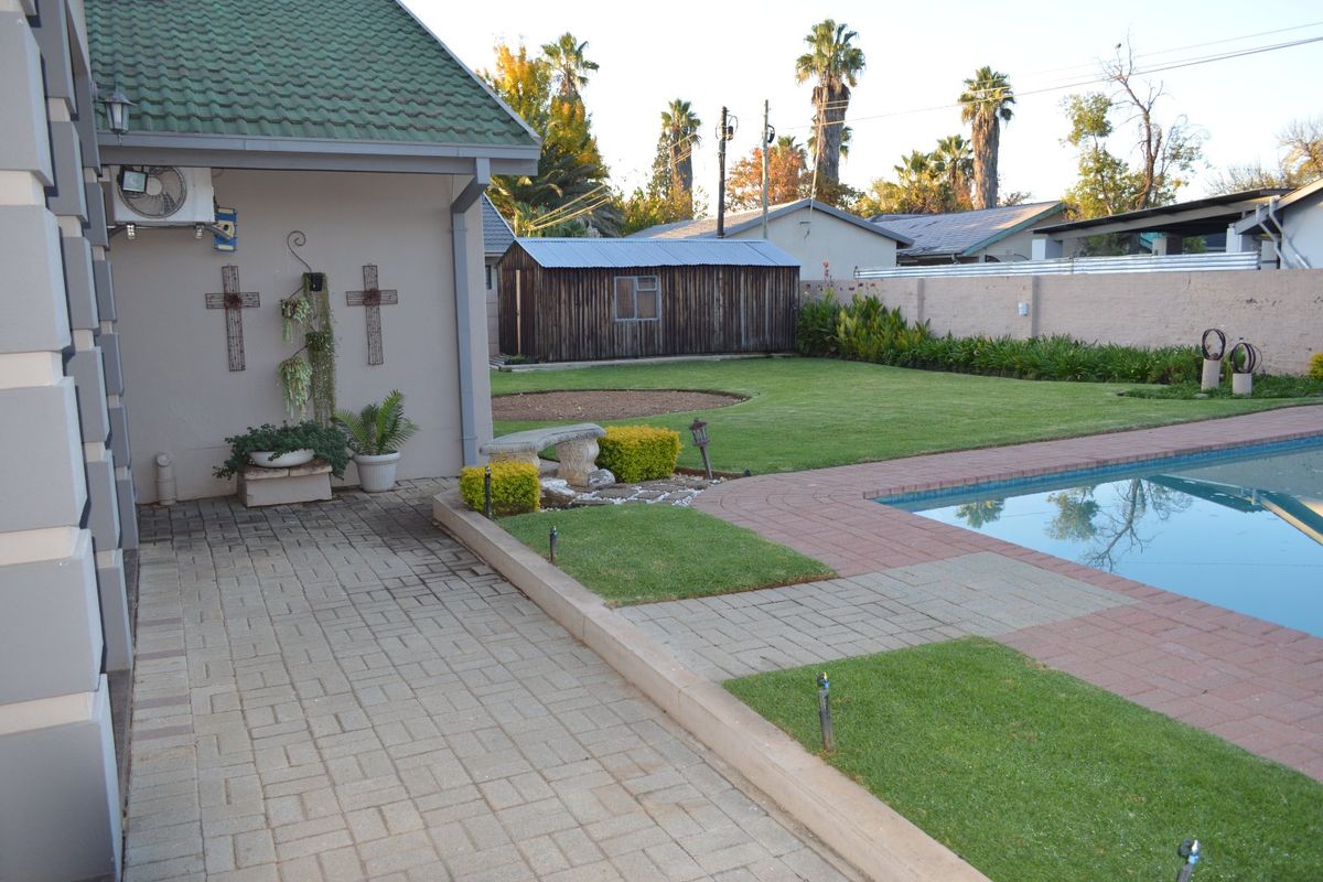 Rear garden area featuring a swimming pool, paved patio, landscaped lawn, and a detached wooden storage shed.