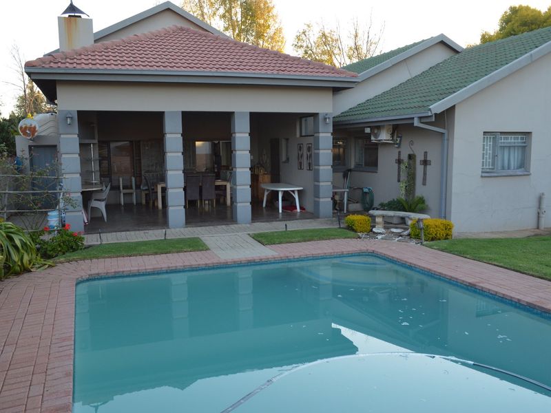 Rear exterior view featuring a swimming pool with brick coping, adjacent to a covered patio area with concrete pillars and tiled roofing.