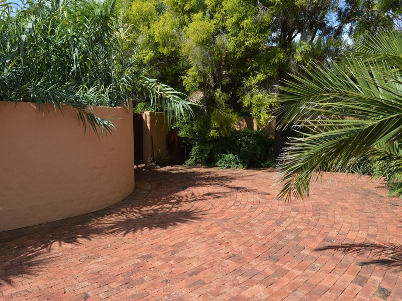 A private garden area featuring circular brick paving, a curved retaining wall, and established mature trees and palms.