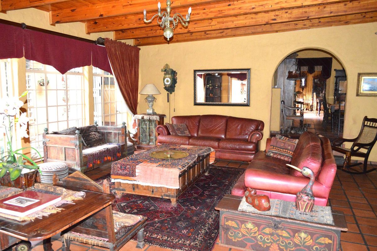 Spacious living room featuring rustic exposed timber ceiling beams, traditional terracotta floor tiles, and an arched entryway leading to adjacent living spaces.