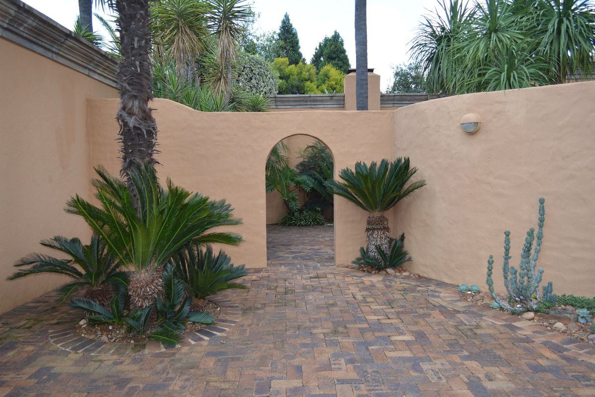 A private, paved courtyard featuring an arched gateway, textured boundary walls, and established landscaping, providing a tranquil outdoor space.