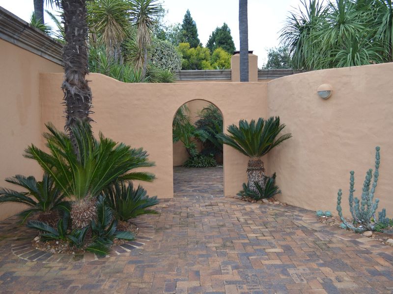 A private, paved courtyard featuring an arched gateway, textured boundary walls, and established landscaping, providing a tranquil outdoor space.