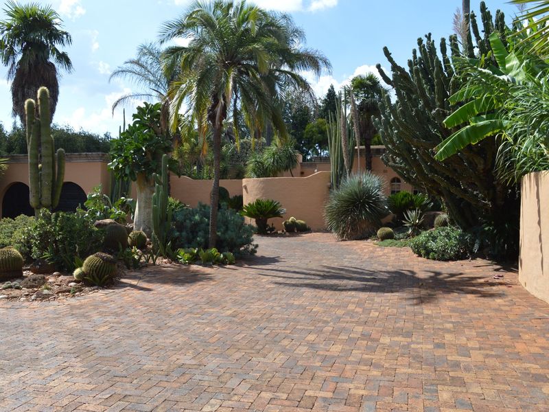 A well-maintained front entrance featuring a brick-paved driveway and established desert-style landscaping with a curved boundary wall.