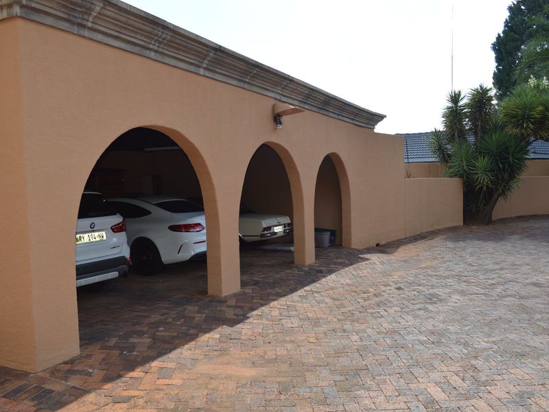 A spacious covered carport featuring distinctive arched masonry pillars and a durable paved driveway, providing ample sheltered parking space.