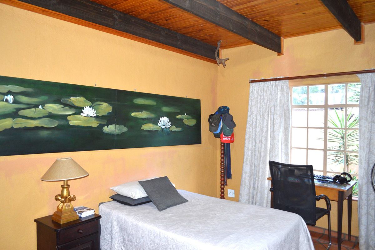 A bedroom featuring exposed timber ceiling beams, textured walls, and a window providing natural light.