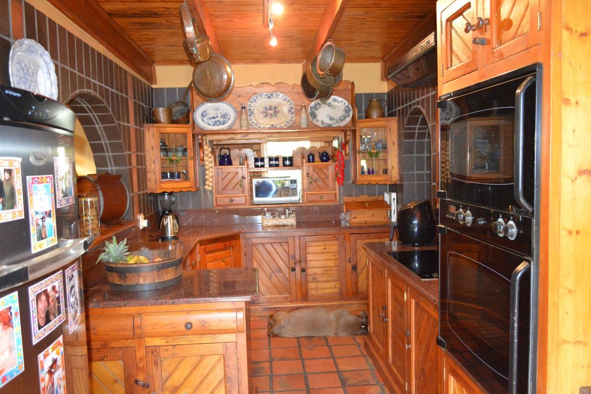 A rustic-style kitchen featuring extensive wooden cabinetry, granite countertops, built-in appliances, and traditional terracotta flooring with a warm timber-clad ceiling.