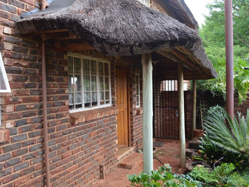 A rustic exterior view featuring a traditional thatched roof, exposed brick walls, and a paved patio area with timber support posts.