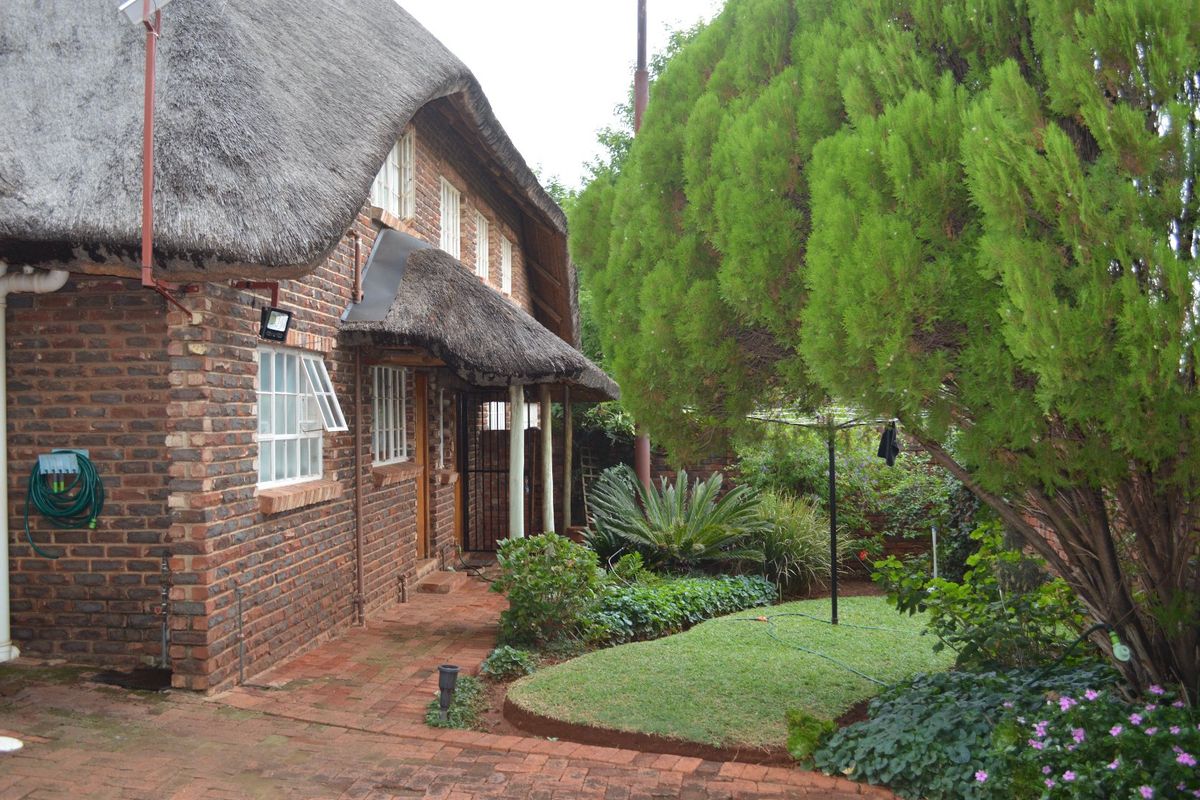 A rear view of a charming face brick house featuring a traditional thatch roof, paved patio area, and a well-maintained garden.