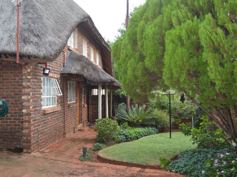 A rear view of a charming face brick house featuring a traditional thatch roof, paved patio area, and a well-maintained garden.