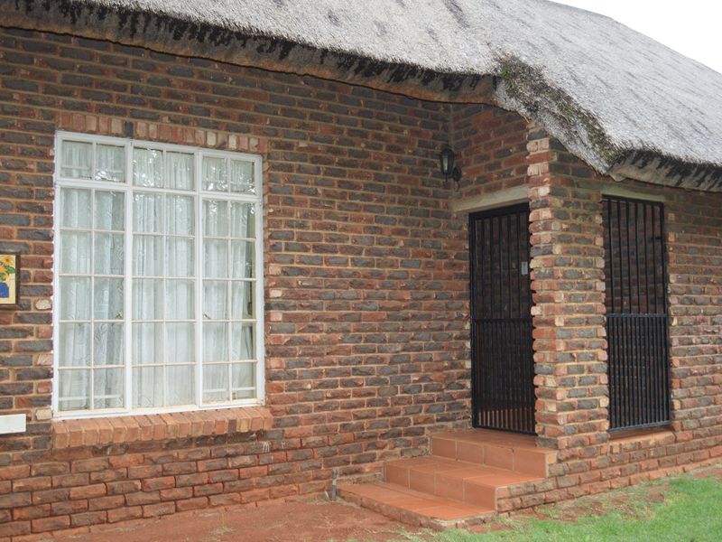 Front facade of a face brick house featuring a traditional thatch roof, security gate, and tiled entrance steps.