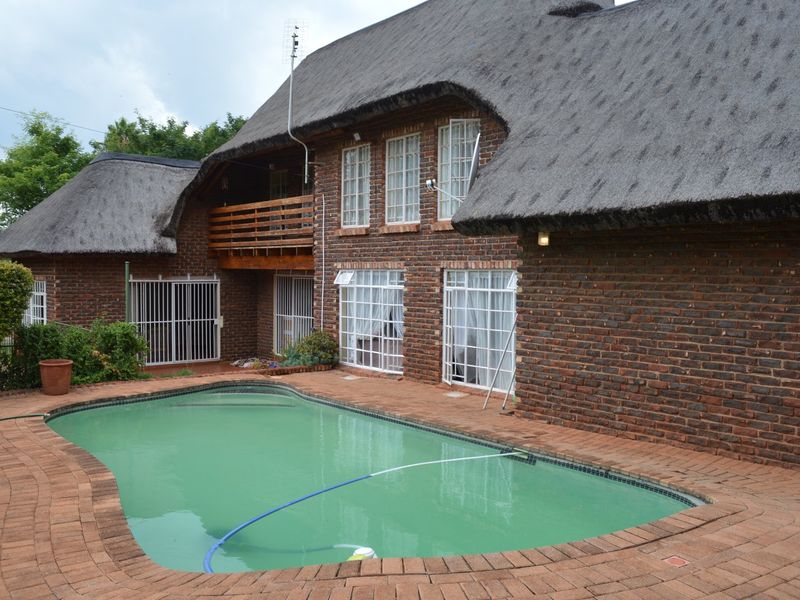 Rear exterior view featuring a swimming pool, brick paving, and a two-story house with a traditional thatched roof and balcony.