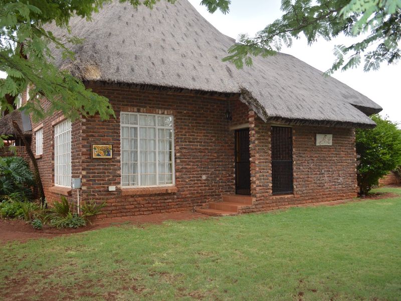 A charming face brick house featuring a traditional thatch roof, secure entrance gate, and a well-maintained front lawn.
