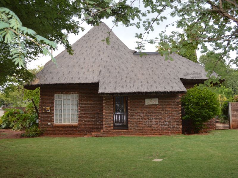 A charming face brick house featuring a traditional thatched roof, set within a well-maintained garden with mature trees.