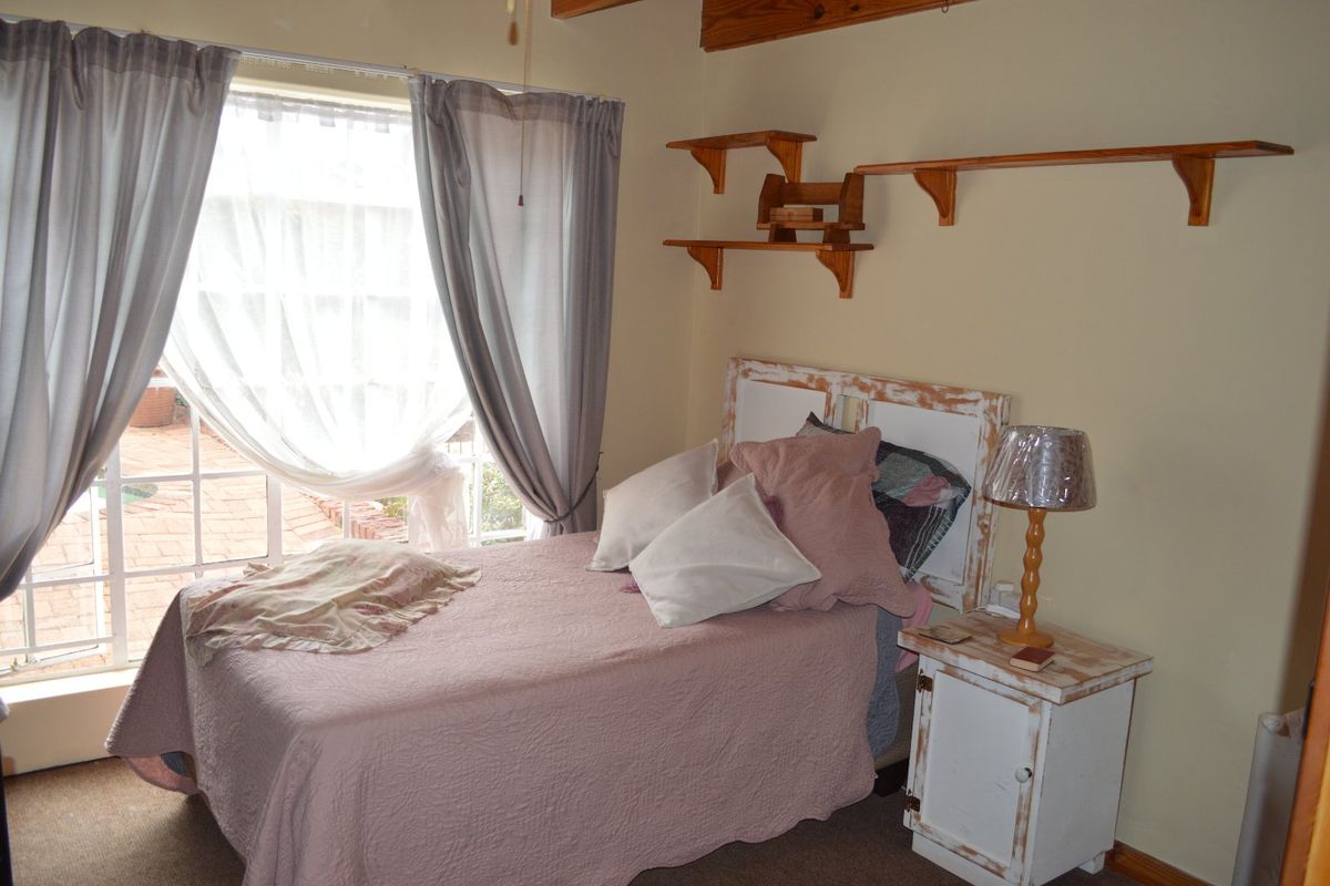 A cozy bedroom featuring exposed timber ceiling beams, built-in wooden wall shelving, and a large window providing natural light.