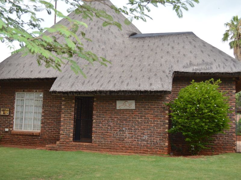 A charming face brick house featuring a traditional thatch roof, set within a well-maintained garden with mature landscaping.