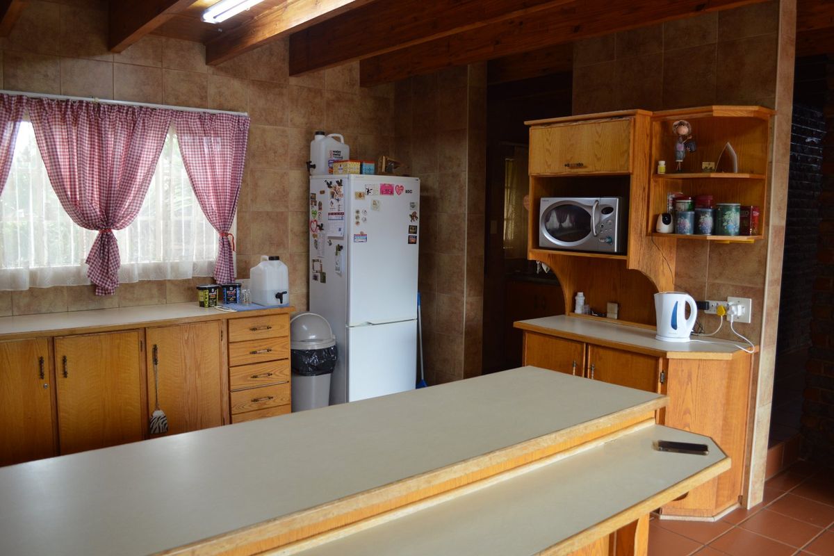 A dated kitchen featuring wooden cabinetry, laminate countertops, and exposed timber ceiling beams with tiled wall finishes.