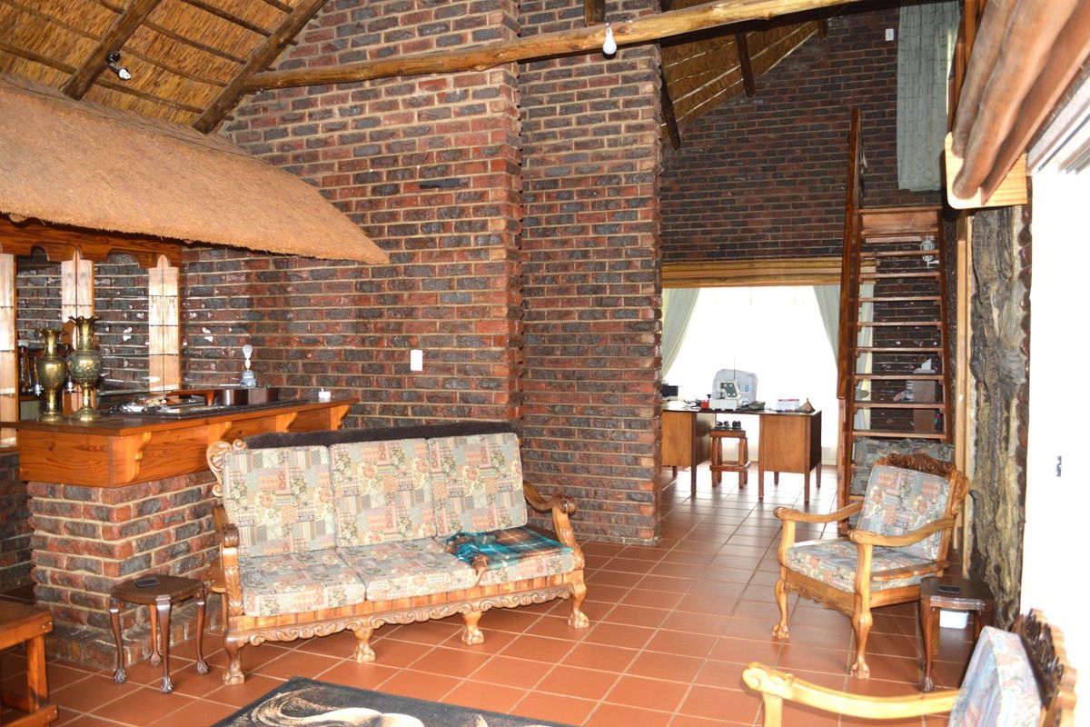 Spacious living area featuring rustic exposed brick walls, a high thatched ceiling, terracotta flooring, and a built-in brick bar with a timber staircase.