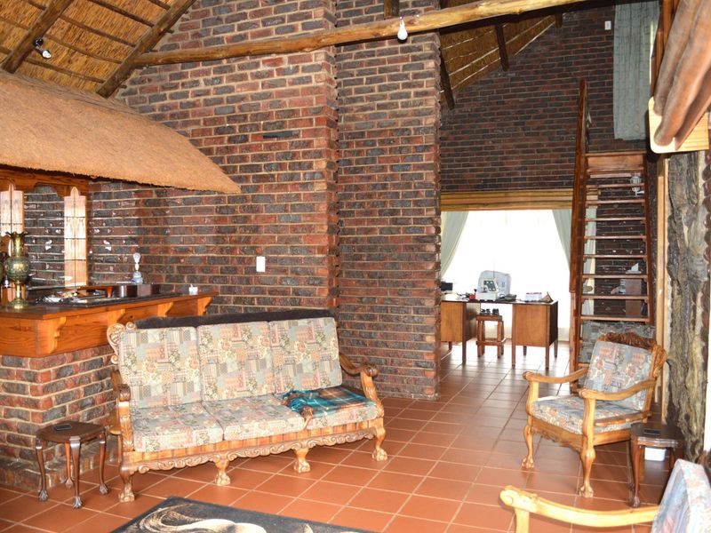 Spacious living area featuring rustic exposed brick walls, a high thatched ceiling, terracotta flooring, and a built-in brick bar with a timber staircase.