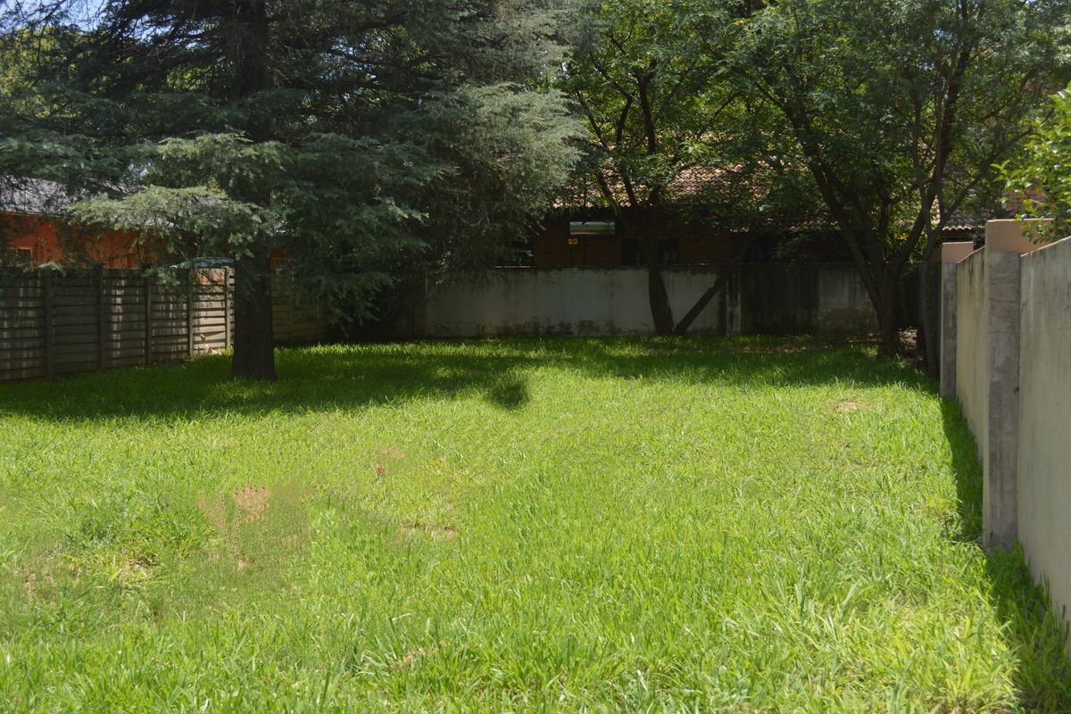 A spacious, level residential plot featuring established trees and secure perimeter boundary walls, offering a private outdoor space.