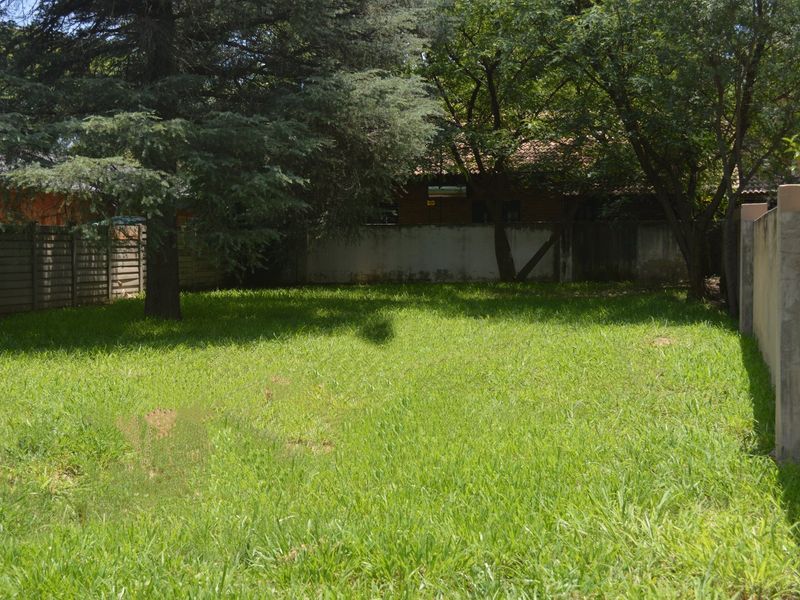 A spacious, level residential plot featuring established trees and secure perimeter boundary walls, offering a private outdoor space.