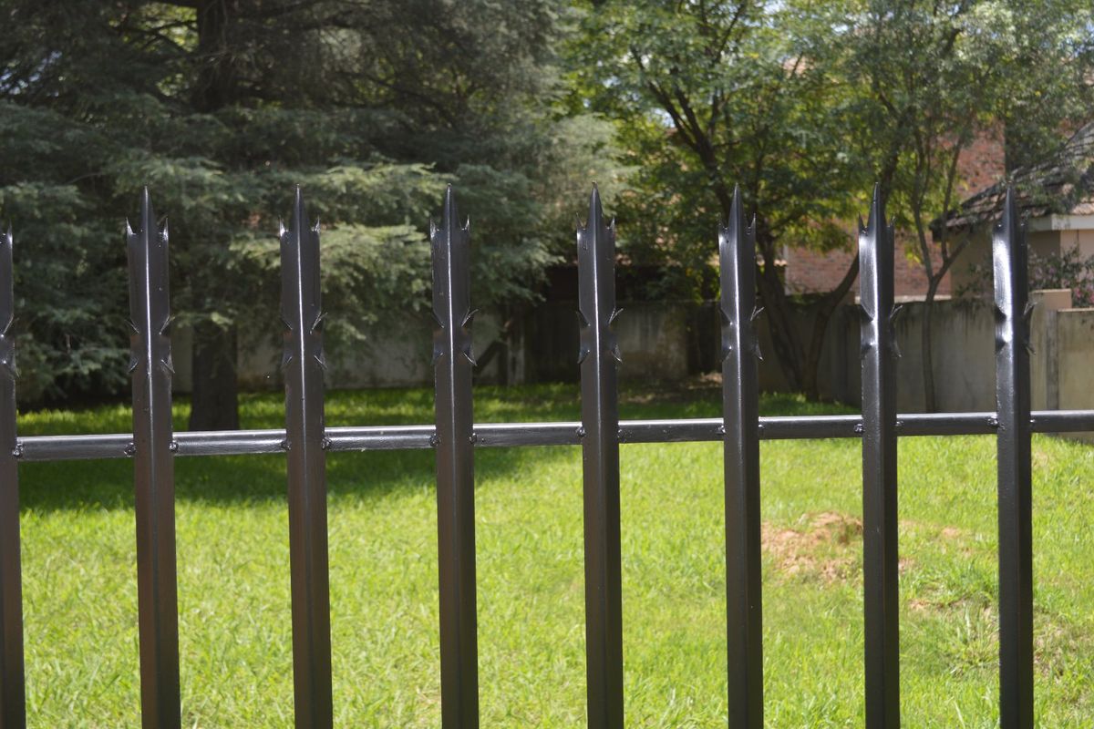 A view of a well-maintained garden area secured by black metal fencing with decorative spiked toppers.