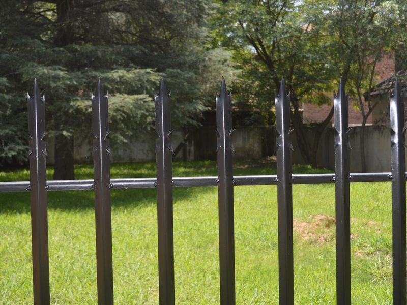 A view of a well-maintained garden area secured by black metal fencing with decorative spiked toppers.