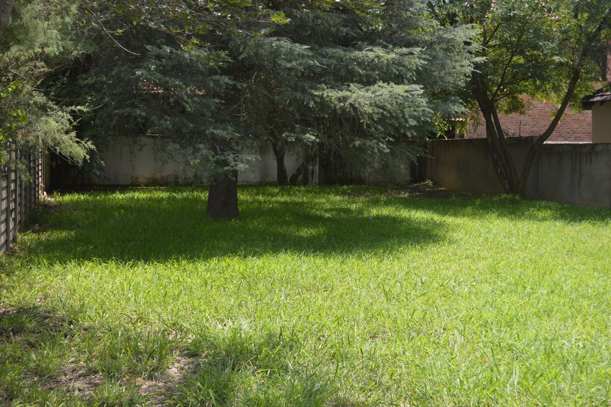 A spacious, grassed garden area featuring mature trees and enclosed by perimeter boundary walls.