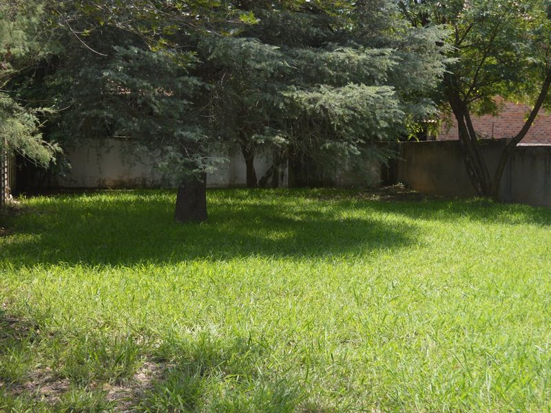 A spacious, grassed garden area featuring mature trees and enclosed by perimeter boundary walls.
