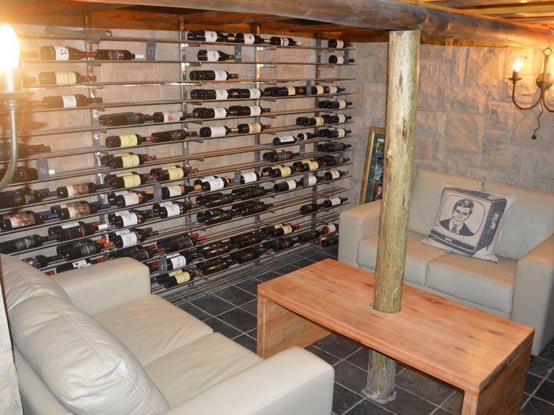 A rustic wine cellar featuring extensive metal racking, stone wall finishes, exposed timber beams, and a central timber support post.
