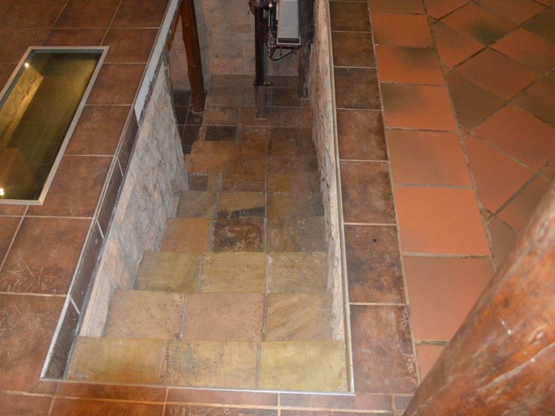 A rustic interior hallway featuring a stone staircase, tiled flooring, and a unique glass floor panel insert, showcasing a farm-style architectural aesthetic.