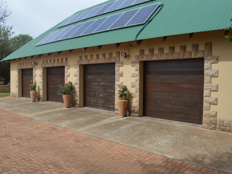 A well-maintained four-car garage featuring stone masonry detailing, dark wood-finish doors, and roof-mounted solar panels, set against a paved driveway.
