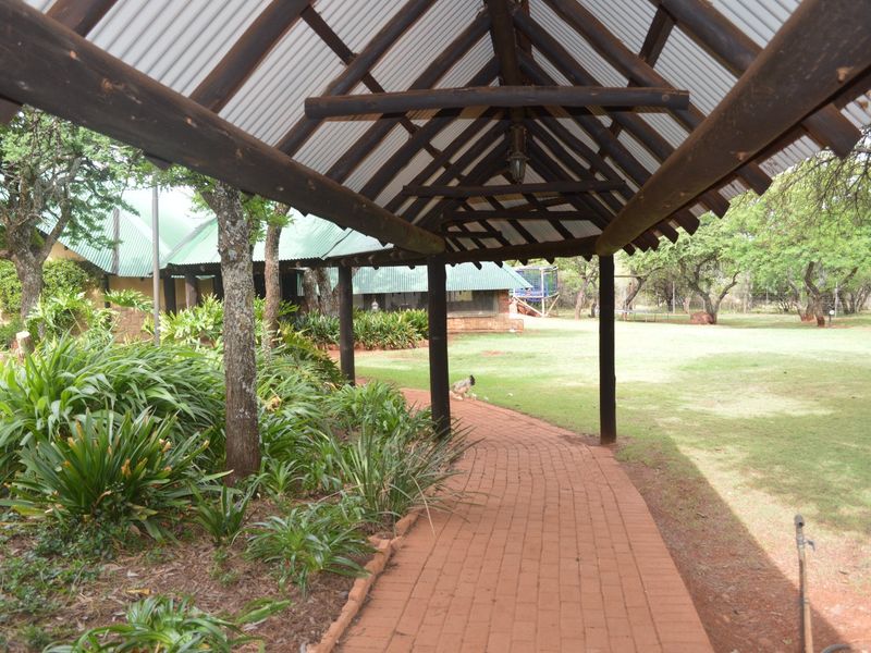 A covered outdoor walkway featuring timber beams and a corrugated roof, leading through a landscaped garden area on the farm property.