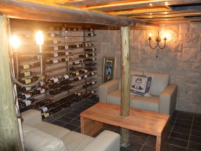 A rustic wine cellar featuring stone-clad walls, exposed timber beams, and integrated metal wine storage racking with tiled flooring.