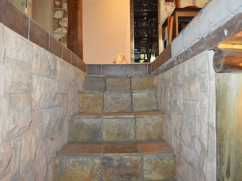 A rustic staircase featuring stone-clad walls and tiled steps, leading to an upper level with a built-in wine cooler.