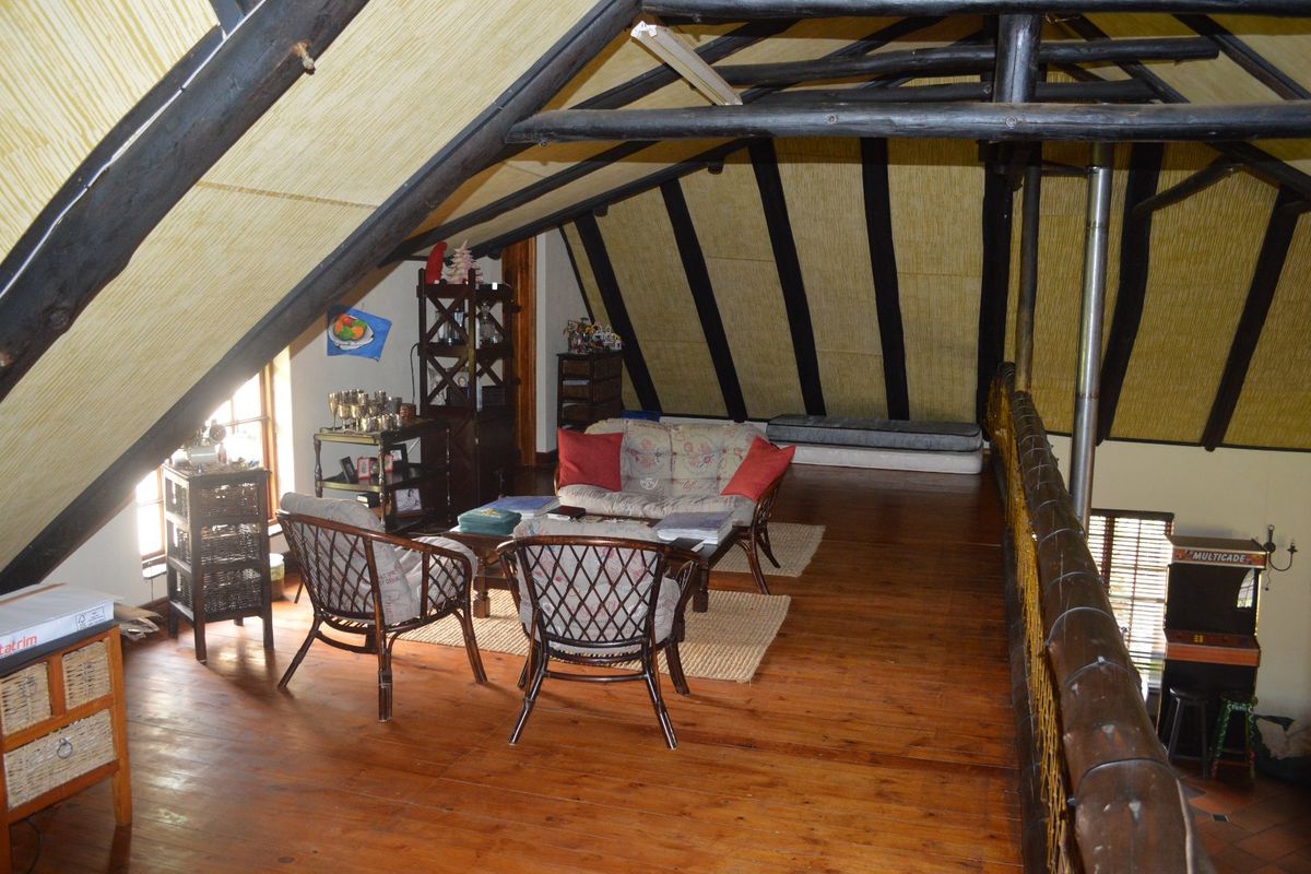 A rustic loft living area featuring exposed timber roof trusses, wooden flooring, and a timber balustrade overlooking the lower level.