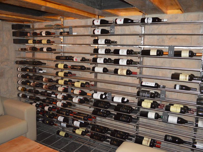 A dedicated wine cellar featuring extensive built-in metal racking, stone wall finishes, and exposed timber ceiling beams, providing a functional storage space for wine collections.