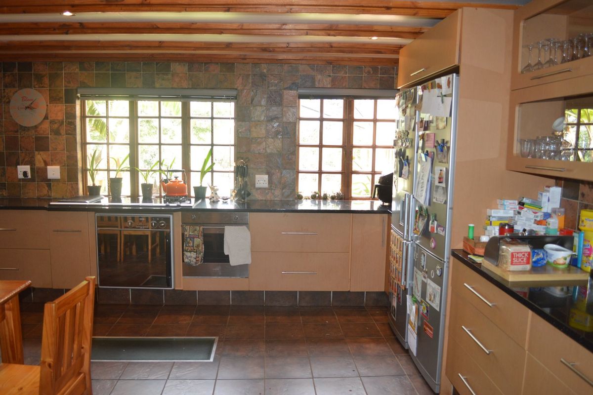 A functional kitchen featuring timber ceiling beams, stone tile backsplash, granite countertops, and built-in cabinetry with integrated oven and hob.