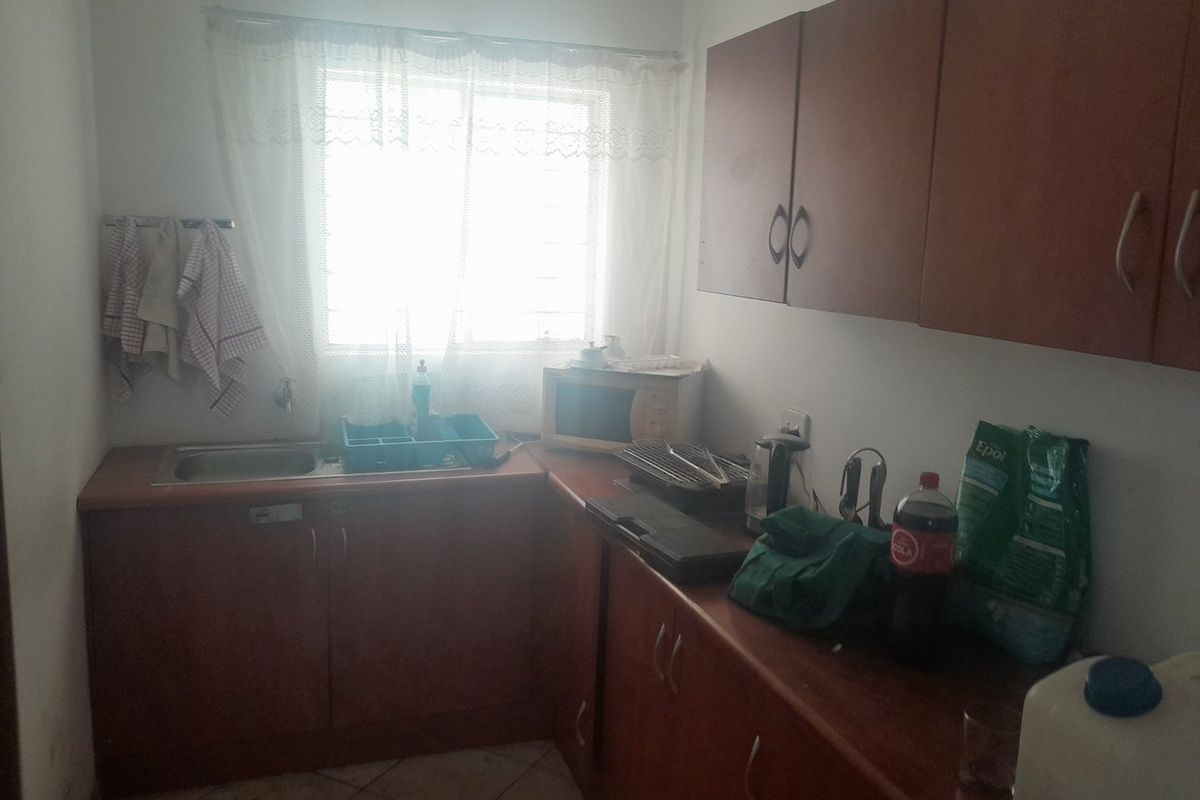 A compact kitchen featuring laminate cabinetry, a stainless steel sink, and tiled flooring, currently showing signs of wear and dated finishes.
