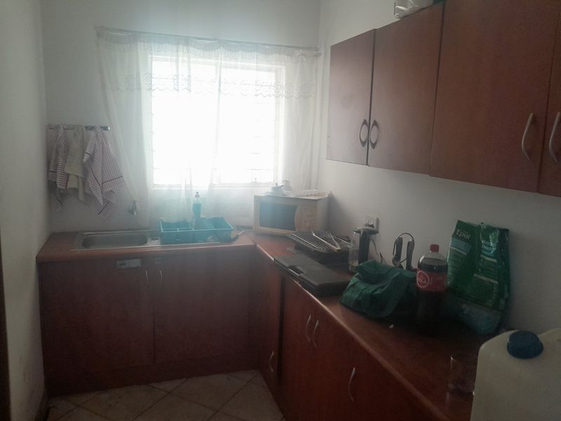 A compact kitchen featuring laminate cabinetry, a stainless steel sink, and tiled flooring, currently showing signs of wear and dated finishes.